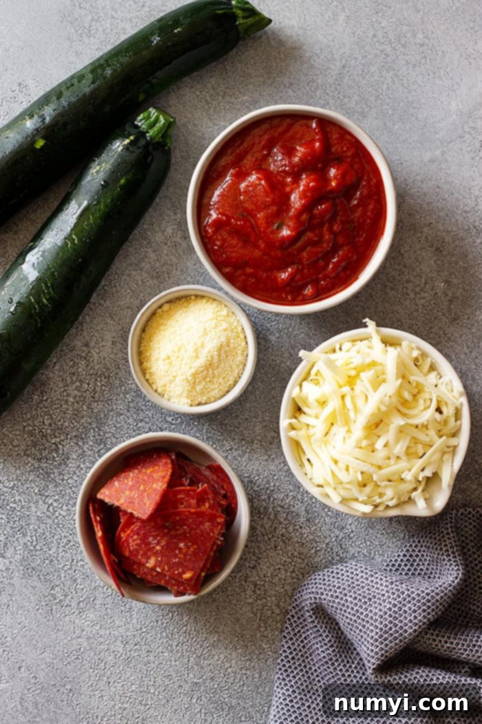 A top down picture of the five simple ingredients needed for zucchini pizza bites: sliced zucchini, pizza sauce, mozzarella cheese, pepperoni, and parmesan cheese.