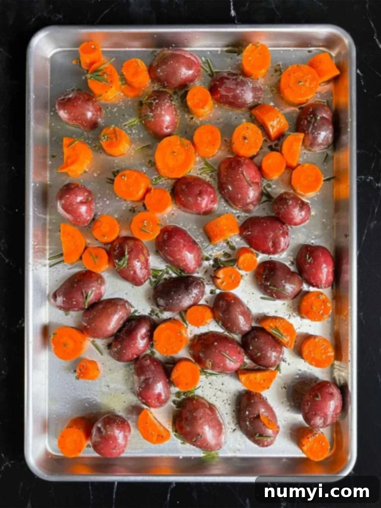 Potatoes and carrots coated with the seasonings, spread into a single layer, on a baking sheet.
