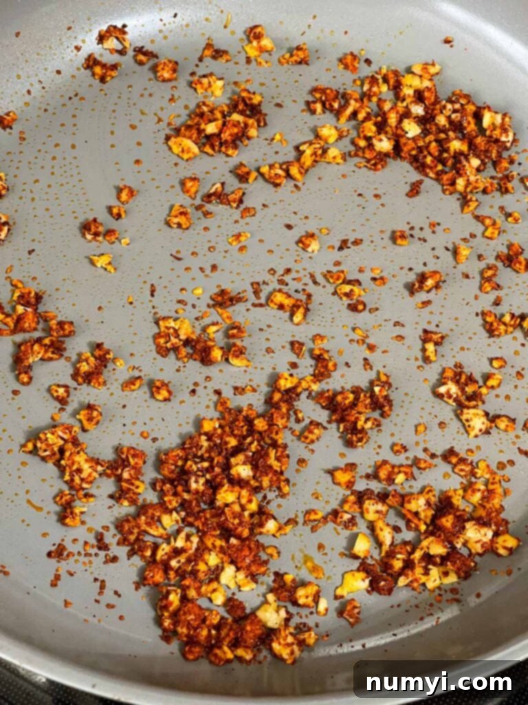 Fiery Garlic Noodle Express 7 Gochugaru chili powder being added to a skillet with ginger and garlic.