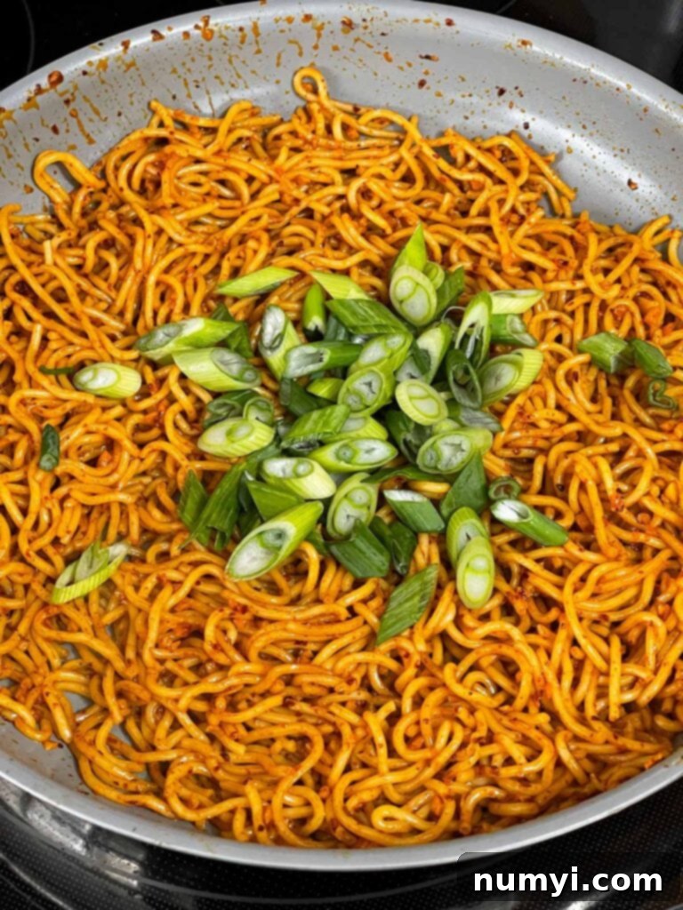 Fiery Garlic Noodle Express 9 Sliced green onions added to spicy garlic noodles in a skillet.