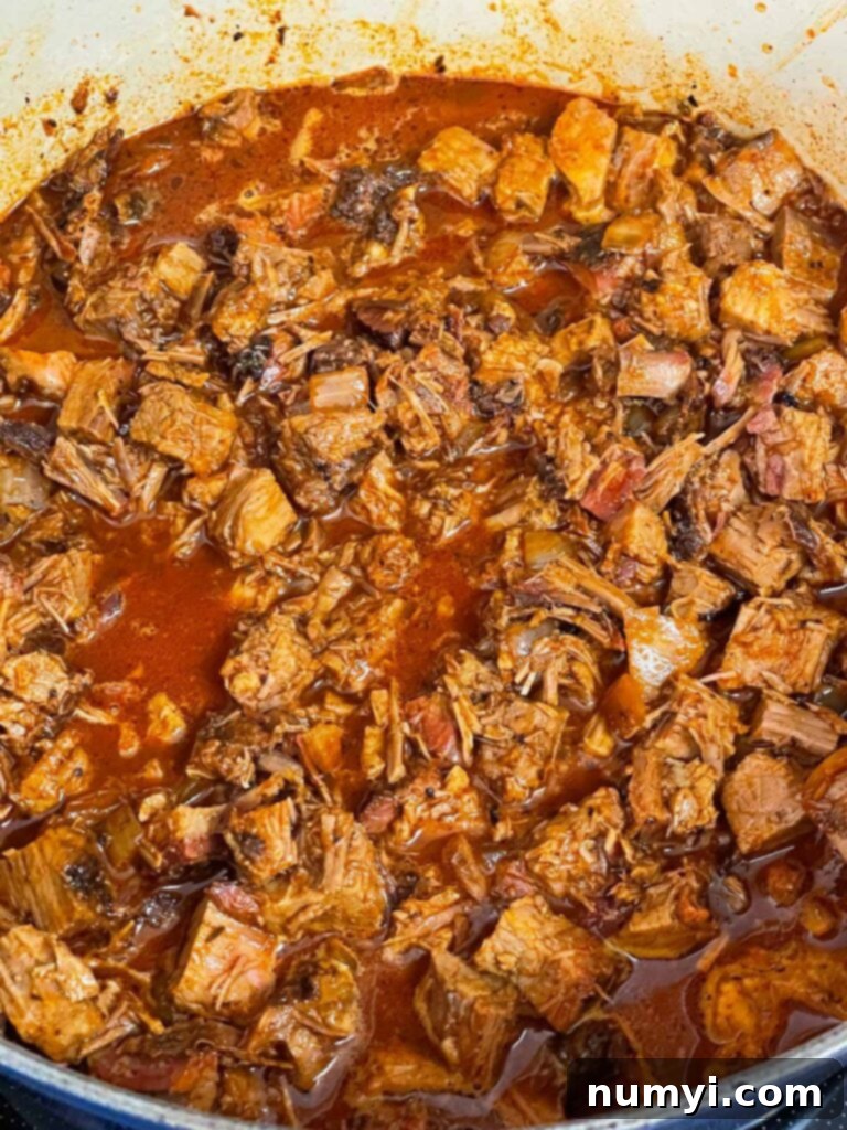 A large pot of rich, dark brisket chili simmering gently in a Dutch oven with the lid slightly ajar, steam escaping. The ingredients are well-combined, creating a thick, aromatic texture.
