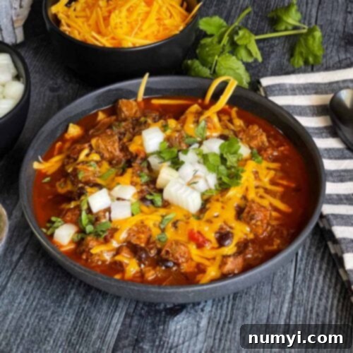 Smoked Brisket Chili, garnished with fresh toppings, in a rustic bowl on a wooden background, ready to be enjoyed.