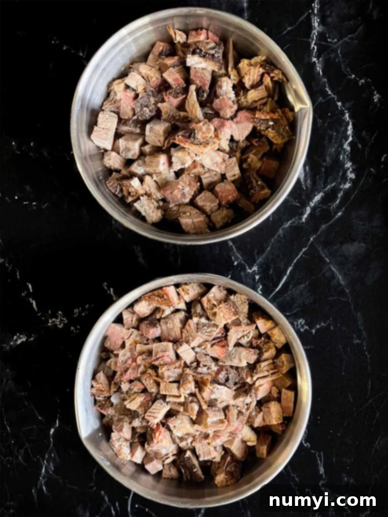Two stainless steel bowls filled with perfectly cubed smoked brisket, ready for use in the chili recipe. The rich color of the smoked meat is visible, indicating its readiness.