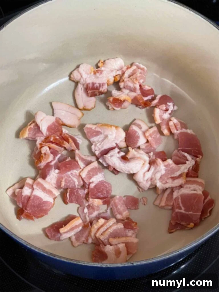 Raw, chopped bacon sizzling in the bottom of a dark blue Dutch oven, rendering its fat.