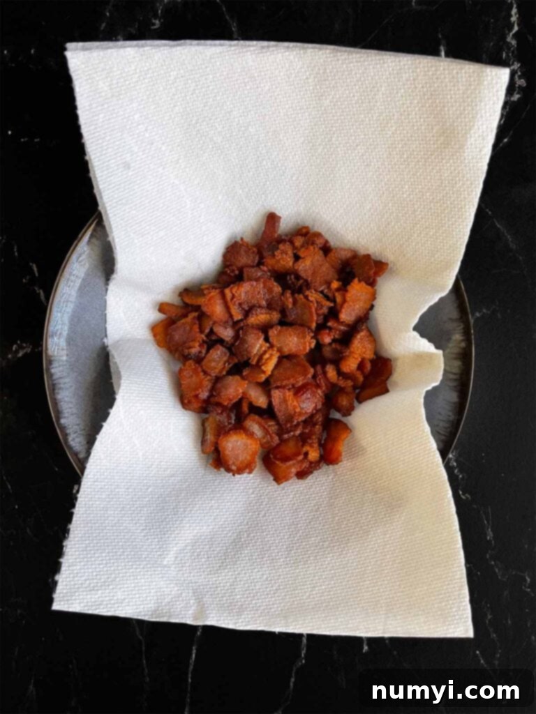 Crispy, cooked bacon pieces draining on paper towels in a small white bowl, ready to be added to the chili later.