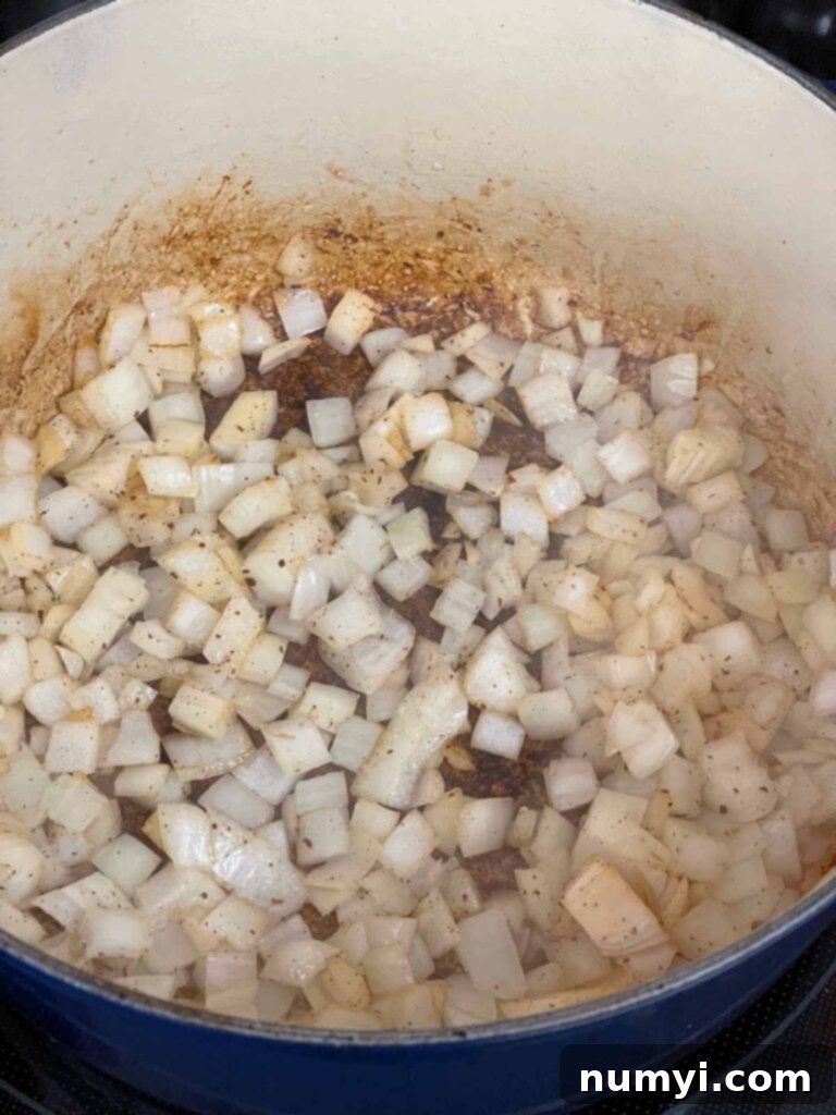 Diced white onions beginning to cook and soften in a dark blue Dutch oven with a small amount of bacon fat.