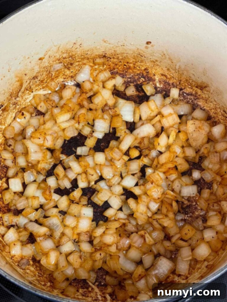 Perfectly cooked, translucent, and lightly browned onions in a Dutch oven, forming the aromatic base for the brisket chili.