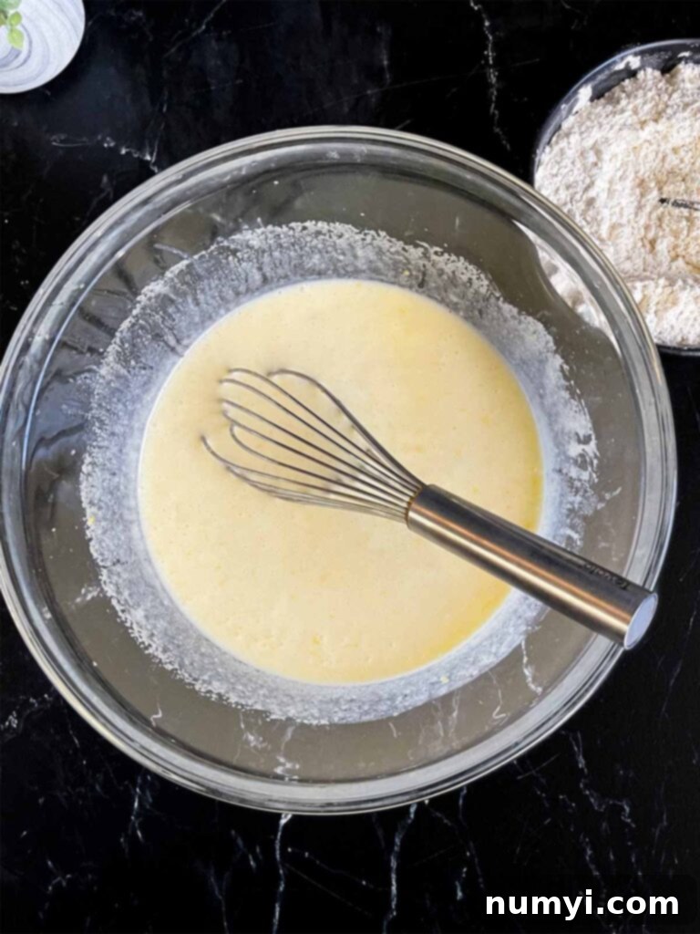 Wet ingredients for the lemon poppy seed muffins whisked together in a glass mixing bowl on a dark surface.