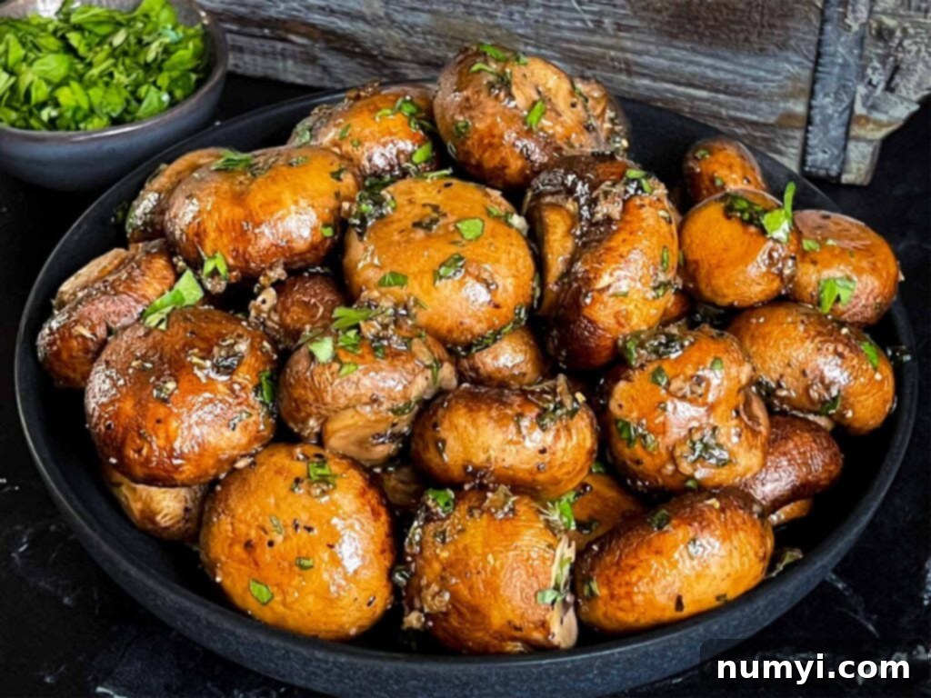 Garlic butter roasted mushrooms in a dark bowl on a dark surface, garnished with fresh parsley.