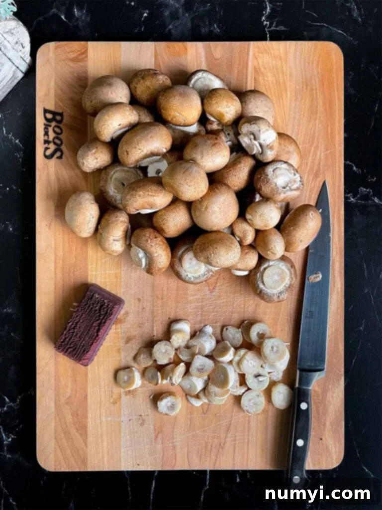 Cleaned and trimmed Cremini (baby bella) mushrooms neatly arranged on a wooden cutting board.