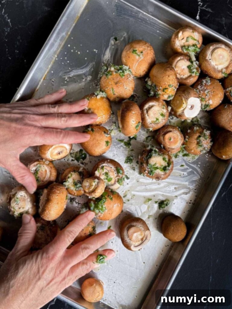 A close-up of mushrooms being tossed with the garlic butter mixture on a baking sheet to ensure even coating.