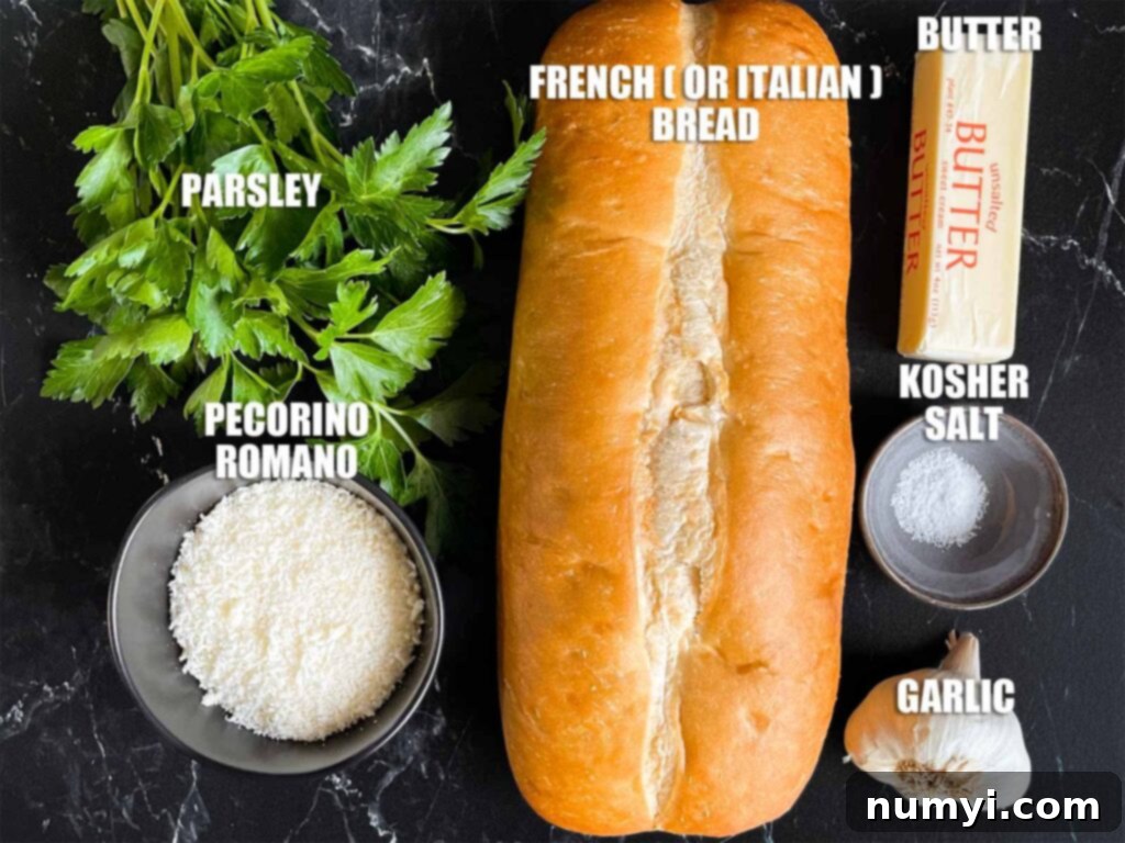 A selection of fresh ingredients including a loaf of Italian bread, garlic cloves, fresh parsley, softened butter, and grated Romano cheese, laid out on a kitchen counter.