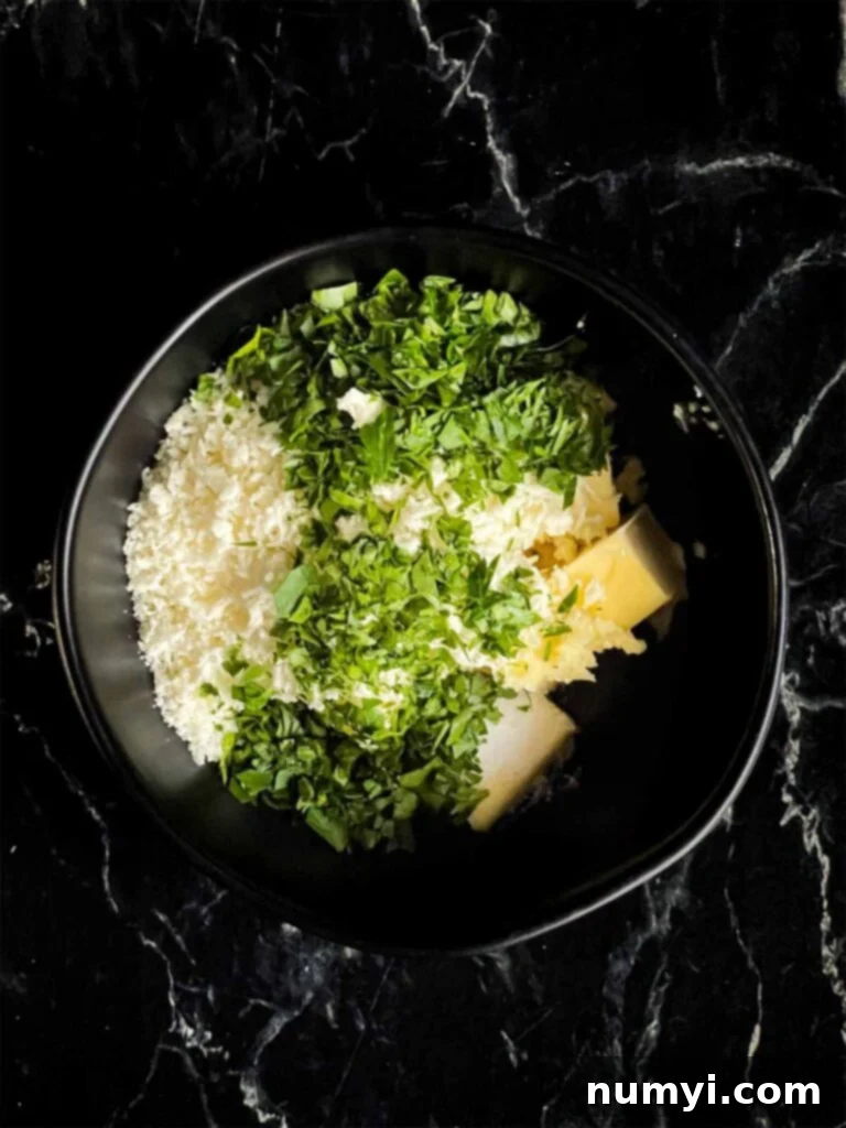 Softened butter and fresh parsley and garlic in a black mixing bowl, before being combined.