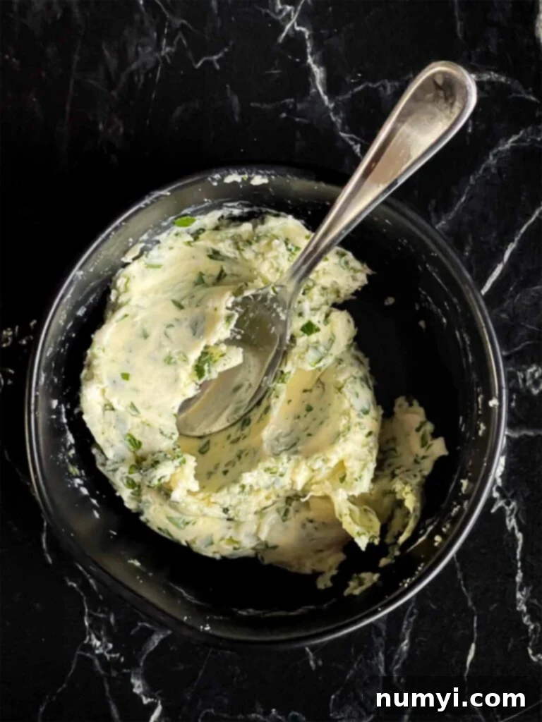 A close-up of fragrant compound butter, a blend of softened butter, minced garlic, and fresh herbs, in a black mixing bowl.