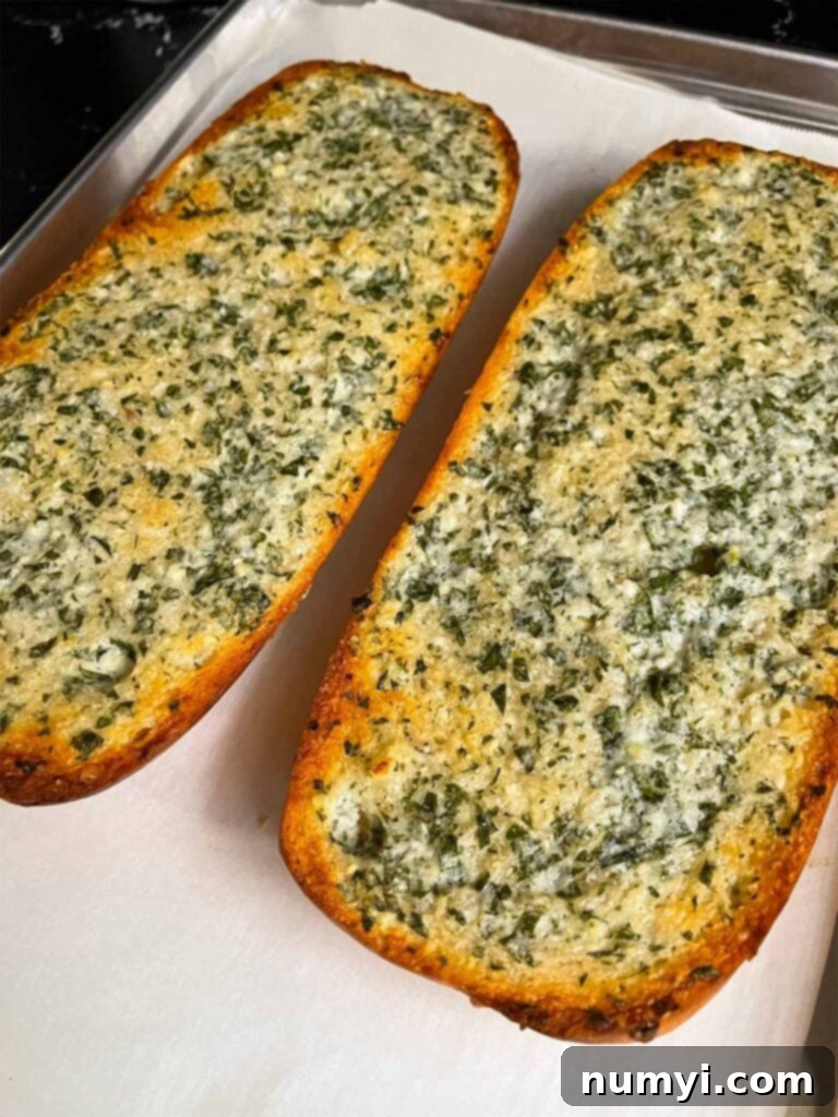 A freshly baked loaf of golden-brown garlic bread, just out of the oven and resting on a parchment-lined baking sheet.