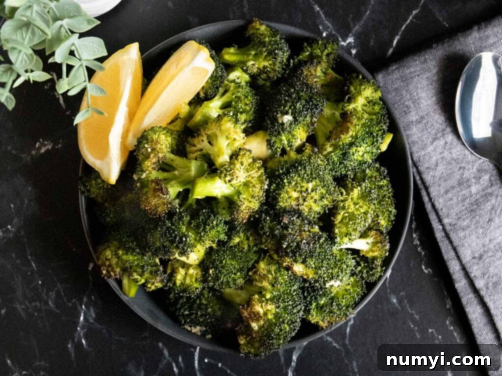 Crispy Oven Roasted Broccoli 2 Roasted broccoli with lemon wedge garnish in a dark bowl.