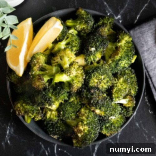 Crispy Oven Roasted Broccoli 8 Roasted broccoli with lemon wedge garnish in a dark bowl.