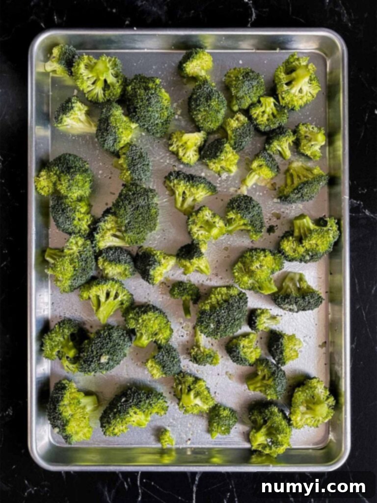Crispy Oven Roasted Broccoli 5 Seasoned broccoli florets on a baking sheet.