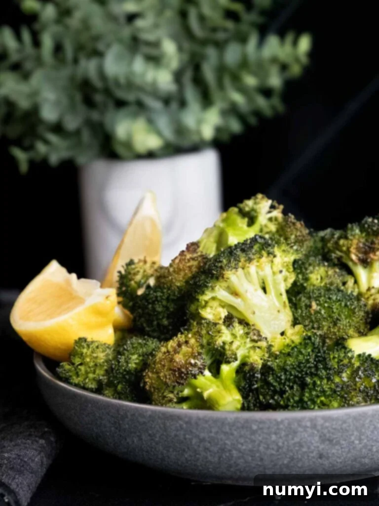 Crispy Oven Roasted Broccoli 7 Roasted broccoli with lemon wedge garnish in a dark bowl.