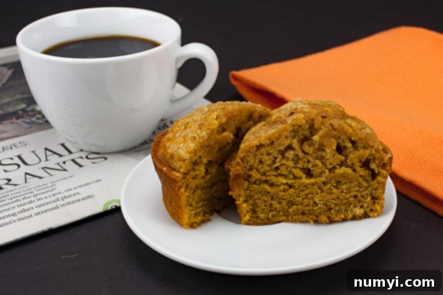 Ultimate Pumpkin Muffins 6 Bakery Style Pumpkin Muffin sliced in half on a white plate next to a white coffee mug, perfect for breakfast.