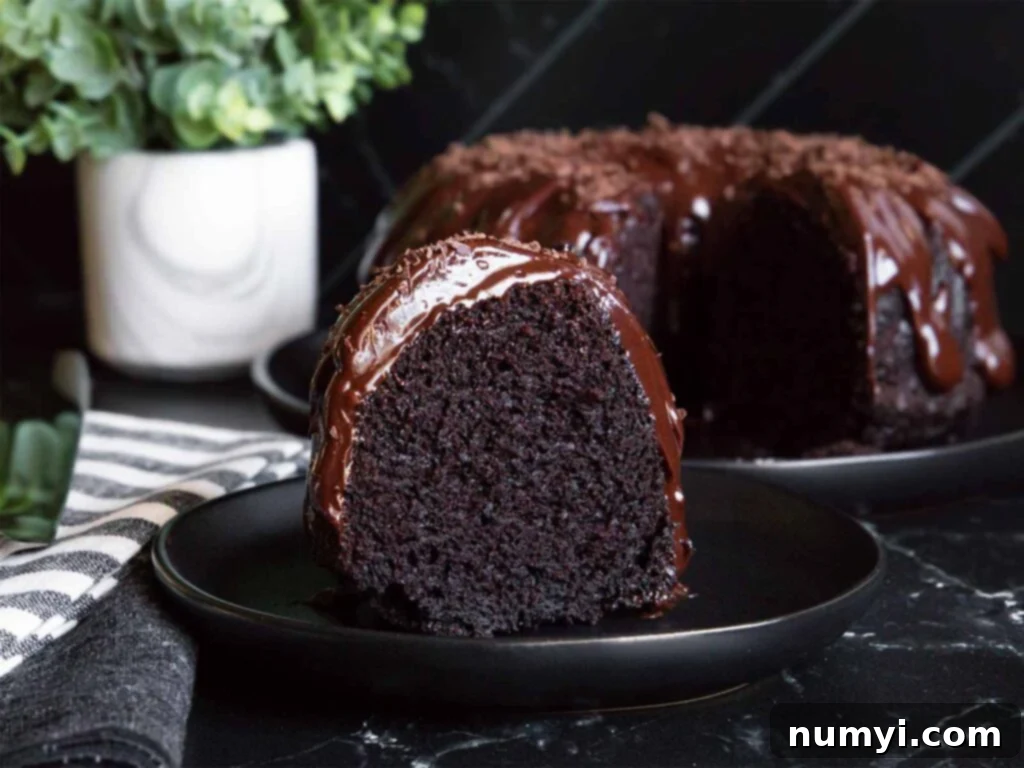 A slice of chocolate bundt cake on a dark plate, showcasing its moist texture and ganache topping.