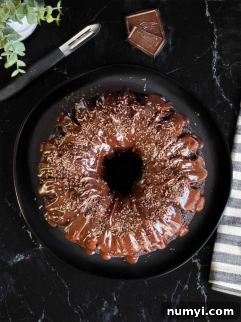 Chocolate bundt cake beautifully topped with chocolate ganache and garnished with chocolate shavings on a dark plate, ready to serve.