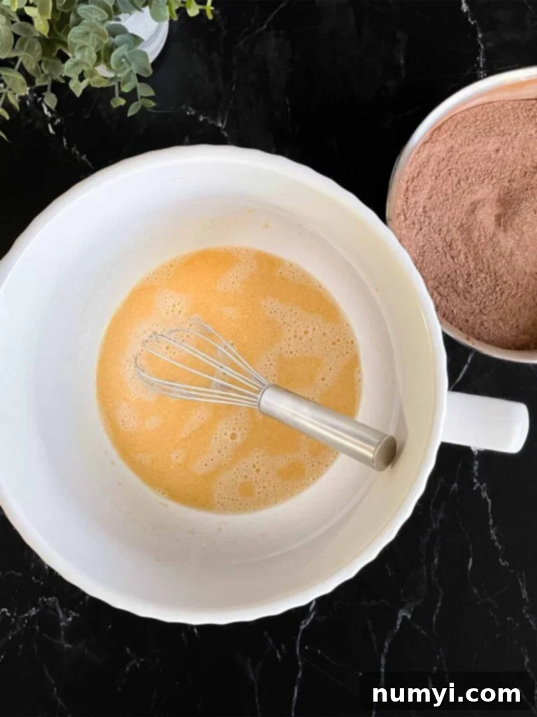 Wet ingredients for chocolate bundt cake recipe in a white mixing bowl on a dark surface.