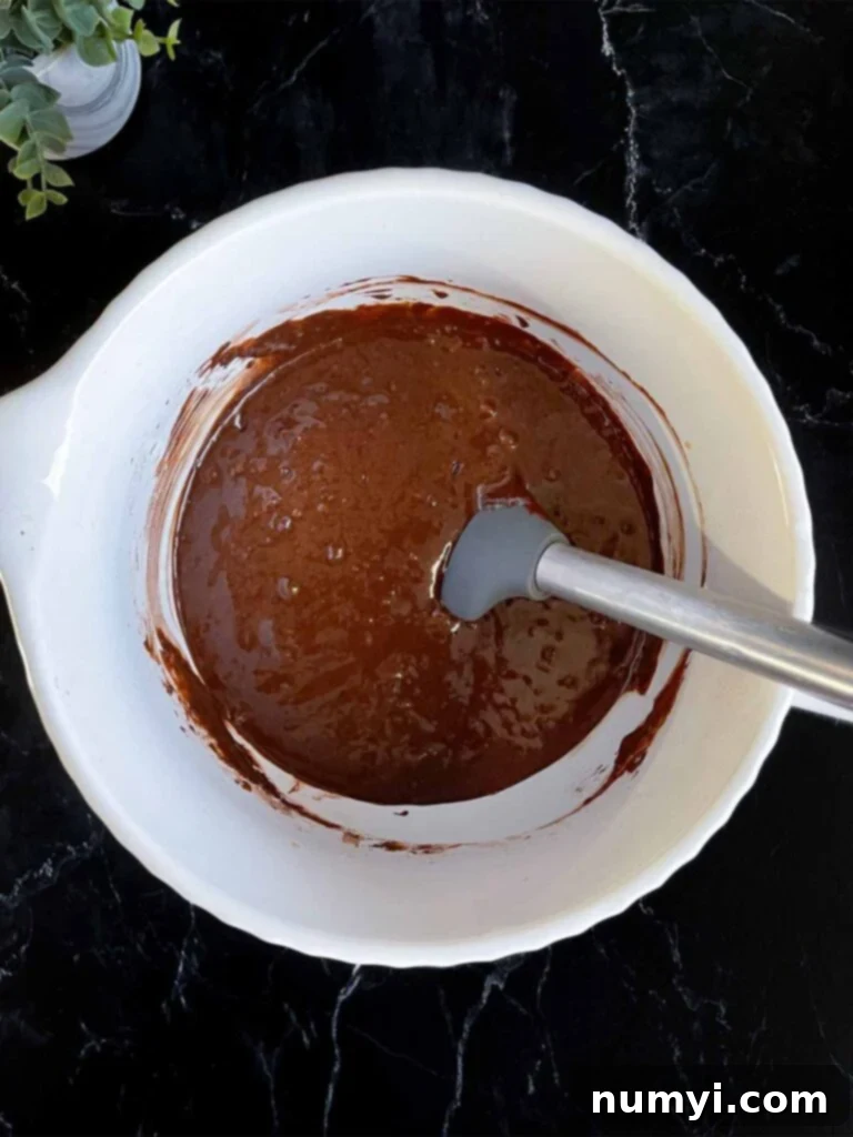 Chocolate bundt cake batter in a large mixing bowl on a dark surface, showing its runny consistency.