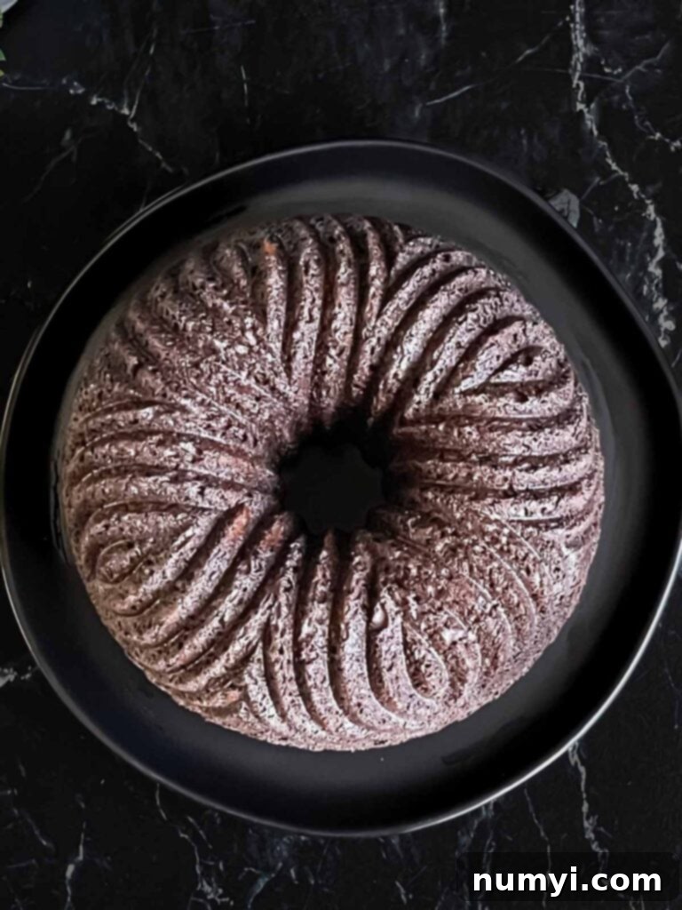 Chocolate bundt cake perfectly inverted onto a dark serving plate, cooling completely.