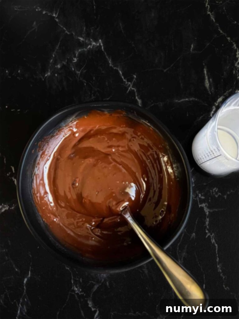 Smooth, glossy chocolate ganache in a small dark bowl on a dark surface.