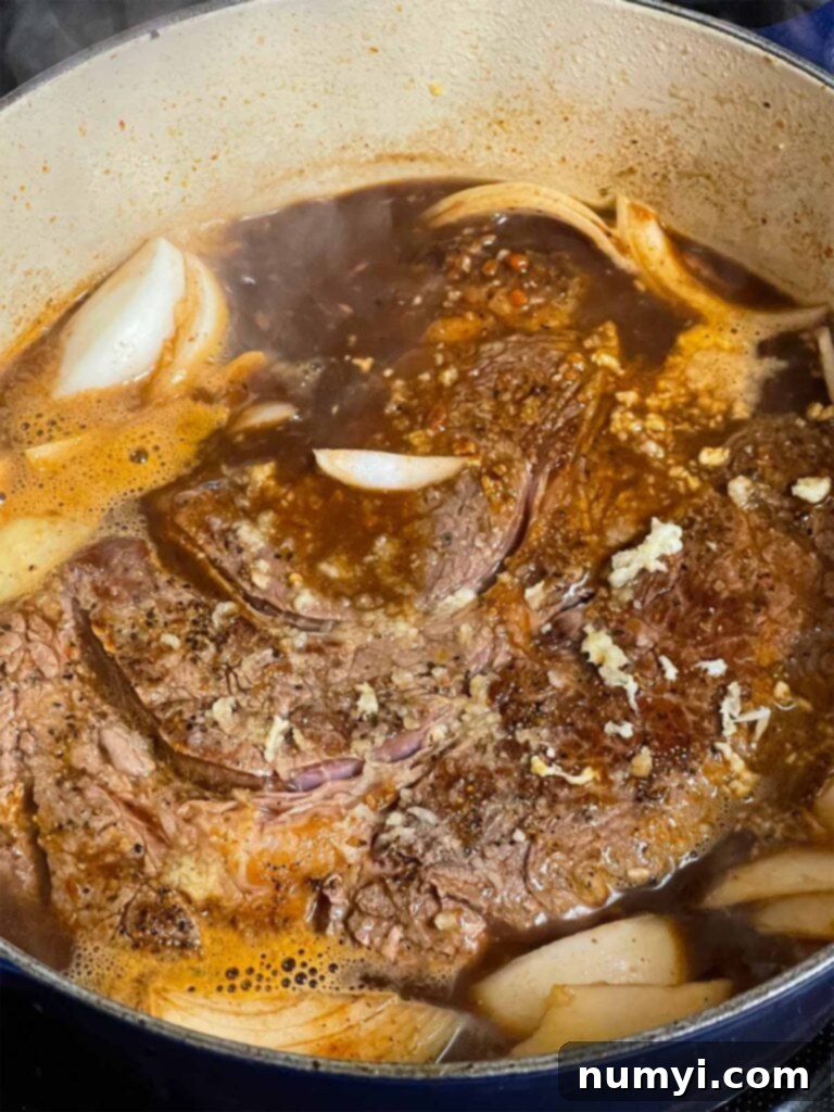 Grandma's Hearty Pot Roast 7 Chuck roast, onion, and garlic added to the beef broth in the dutch oven.