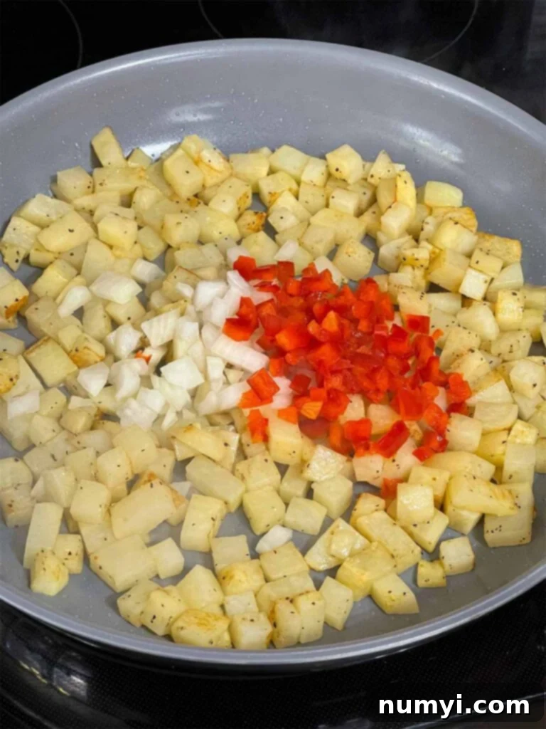 Hearty Smoked Pulled Pork Hash 6 Onions and red bell peppers being added to potatoes in a skillet.