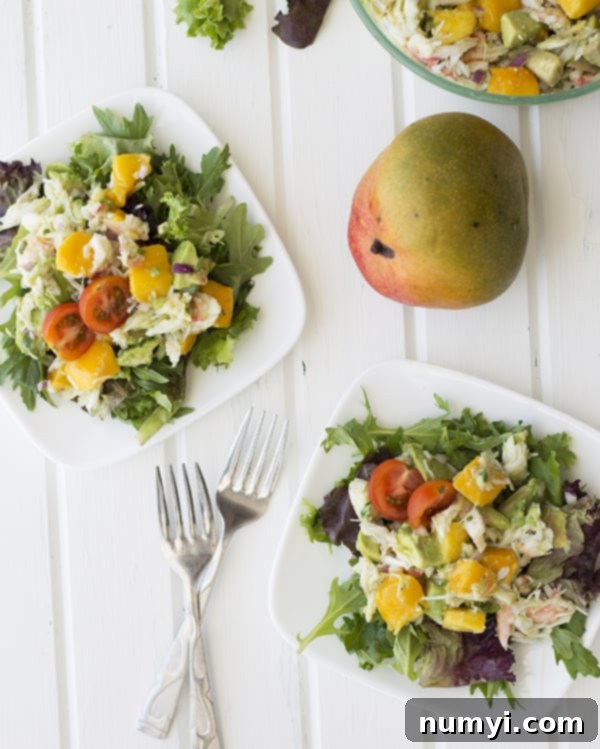 Tropical Crab, Mango, and Avocado Salad 5 Two white plates showcasing elegantly plated servings of crab, mango, and avocado salad on a bed of fresh mixed greens.
