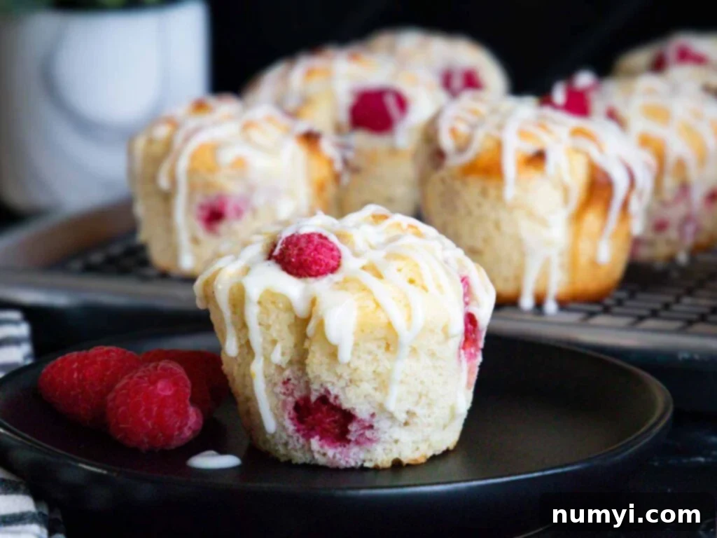 Raspberry muffin on a dark plate garnished with fresh raspberries and lemon zest.