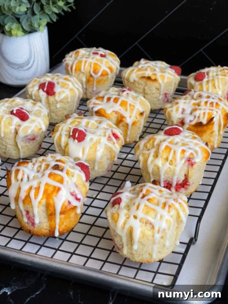 Lemon glazed raspberry muffins on a wire rack over a baking sheet lined with parchment paper.