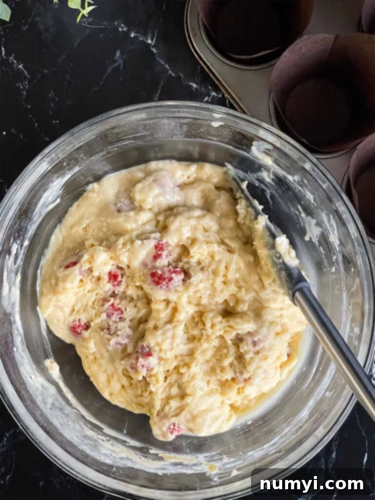Raspberry muffin batter in a glass mixing bowl on a dark surface after resting for 15 minutes.