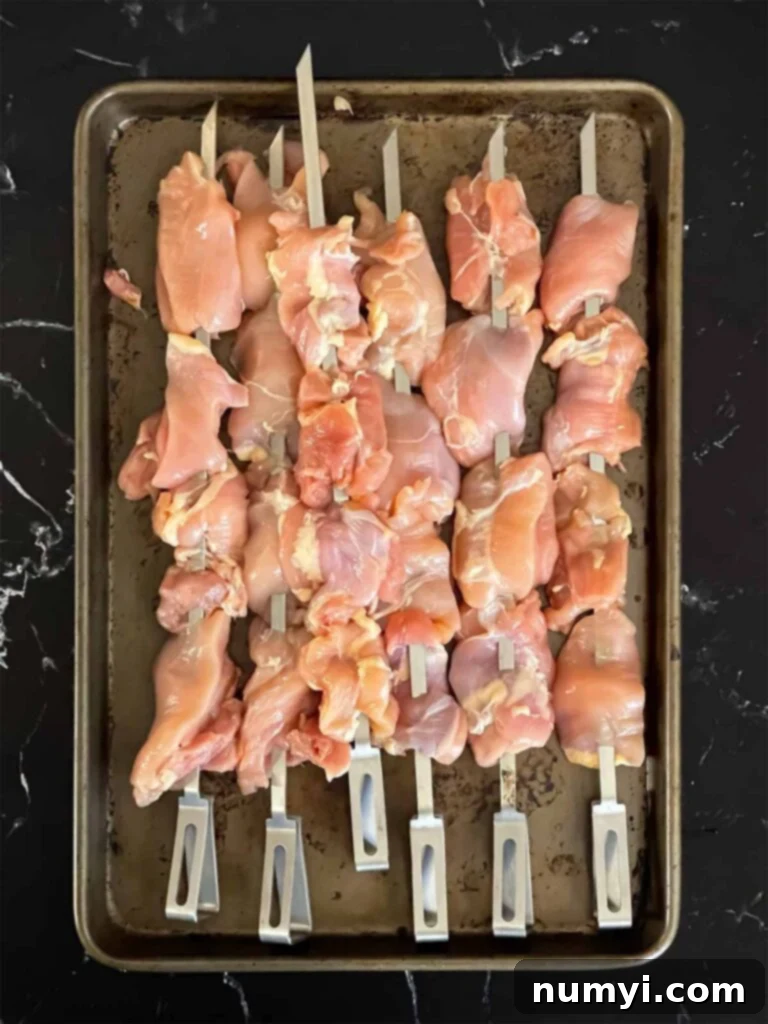 Raw chicken thighs, skewered, on a sheet pan.