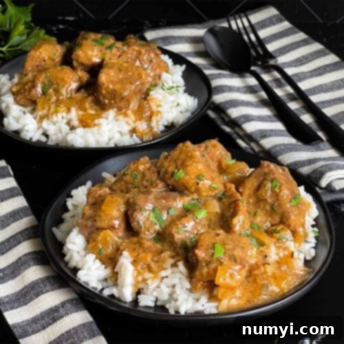 Slow cooker beef tips and gravy over cooked rice on a dark plate on a dark surface.