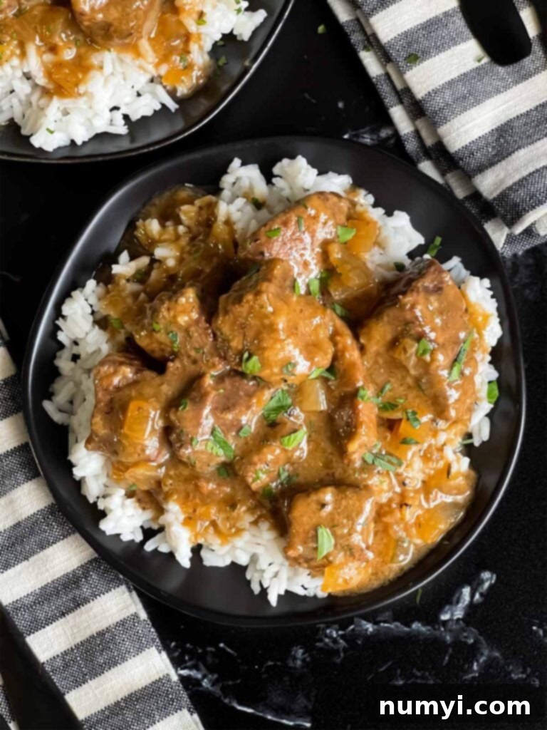 Slow cooker beef tips and gravy over cooked rice on a dark plate on a dark surface.