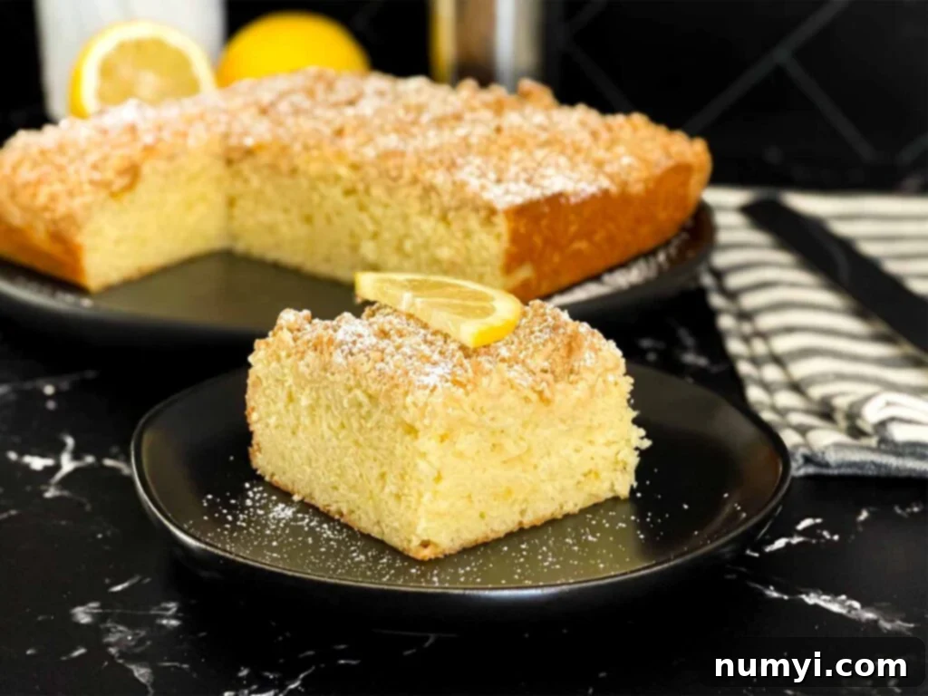 Sunshine Lemon Streusel 2 A slice of lemon crumb cake dusted with powdered sugar and garnished with a lemon slice on a dark plate on a dark surface.