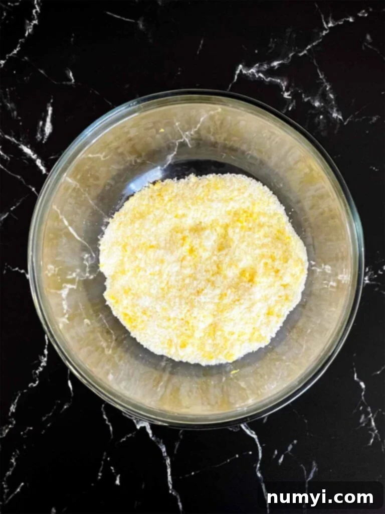 Sunshine Lemon Streusel 6 Lemon zest and granulated sugar rubbed together in a glass mixing bowl for lemon crumb cake recipe.