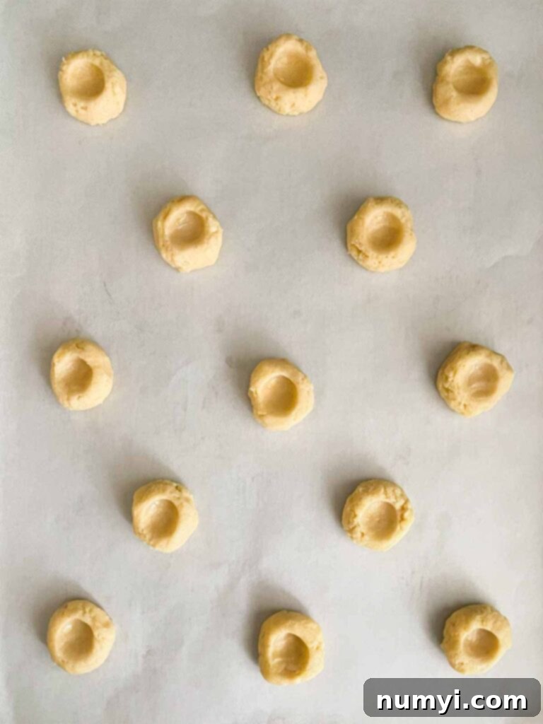 Lemon thumbprint cookie dough with thumb indentations formed on parchment paper lined baking sheet.