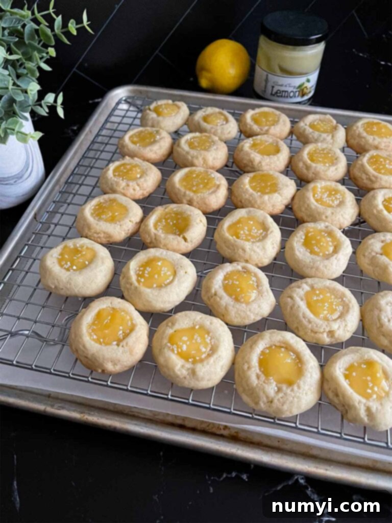 Lemon thumbprint cookies on a wire rack on a dark surface.