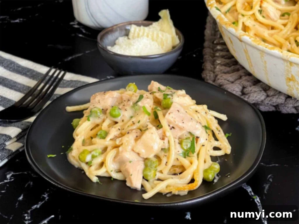 Chicken tetrazzini in a white baking dish with a serving on a dark plate, ready to be enjoyed.
