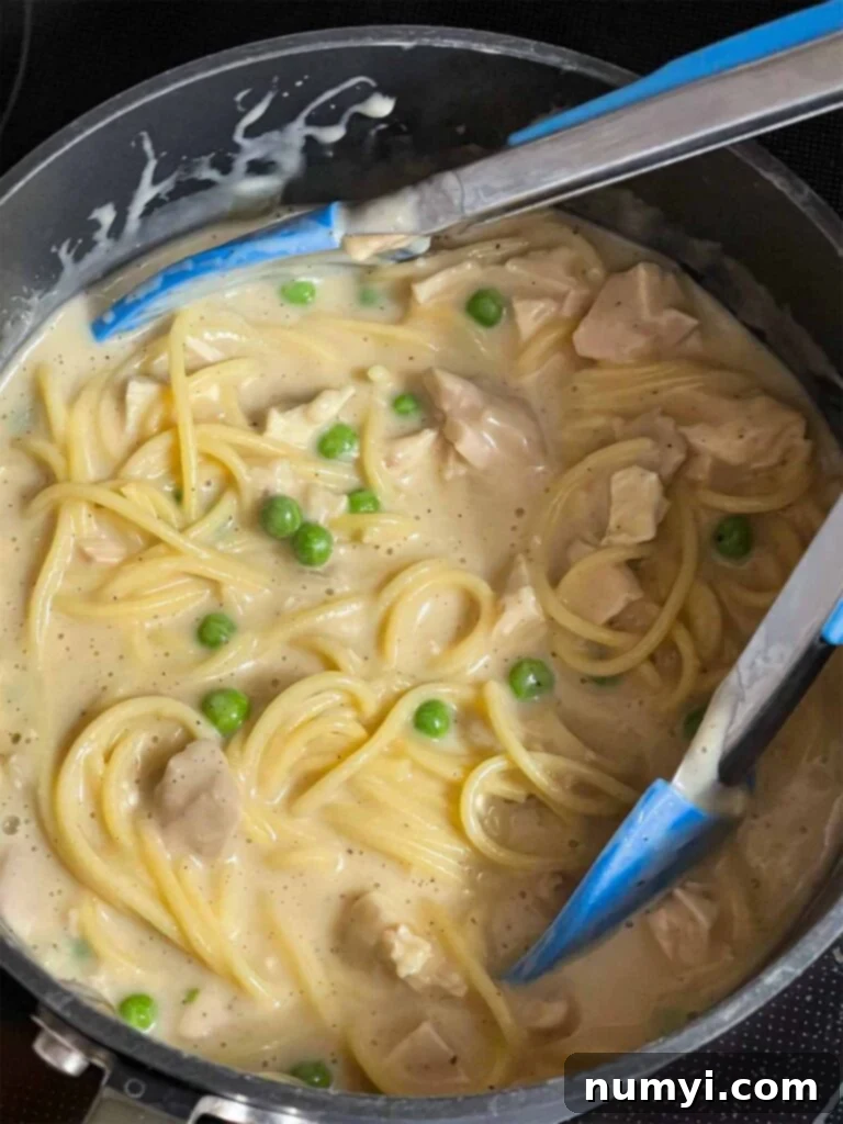 A chicken tetrazzini mixture, with pasta, chicken, and peas, in a large pot.