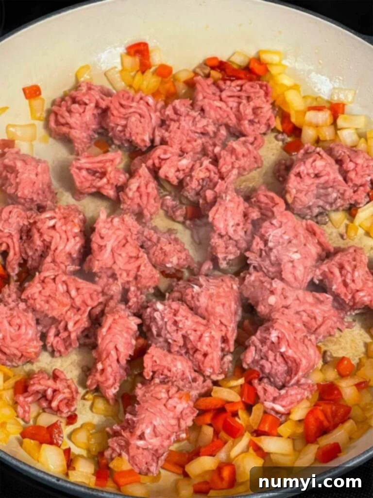 Ground beef added to onions and red bell pepper in a skillet.