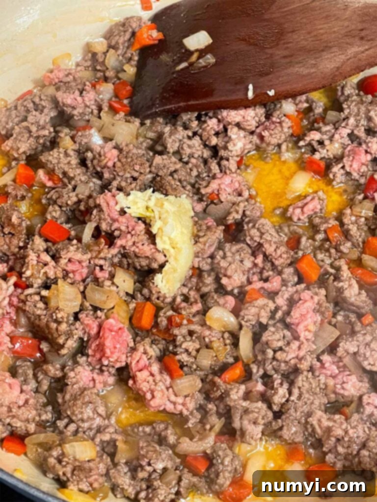 Adding garlic to ground beef, red bell peppers, and onion in a skillet.