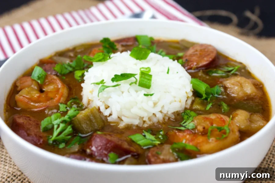 A close-up of a rustic, homemade Shrimp and Sausage Gumbo, served in a white bowl with a generous portion of rice and garnished with fresh green onions and parsley.