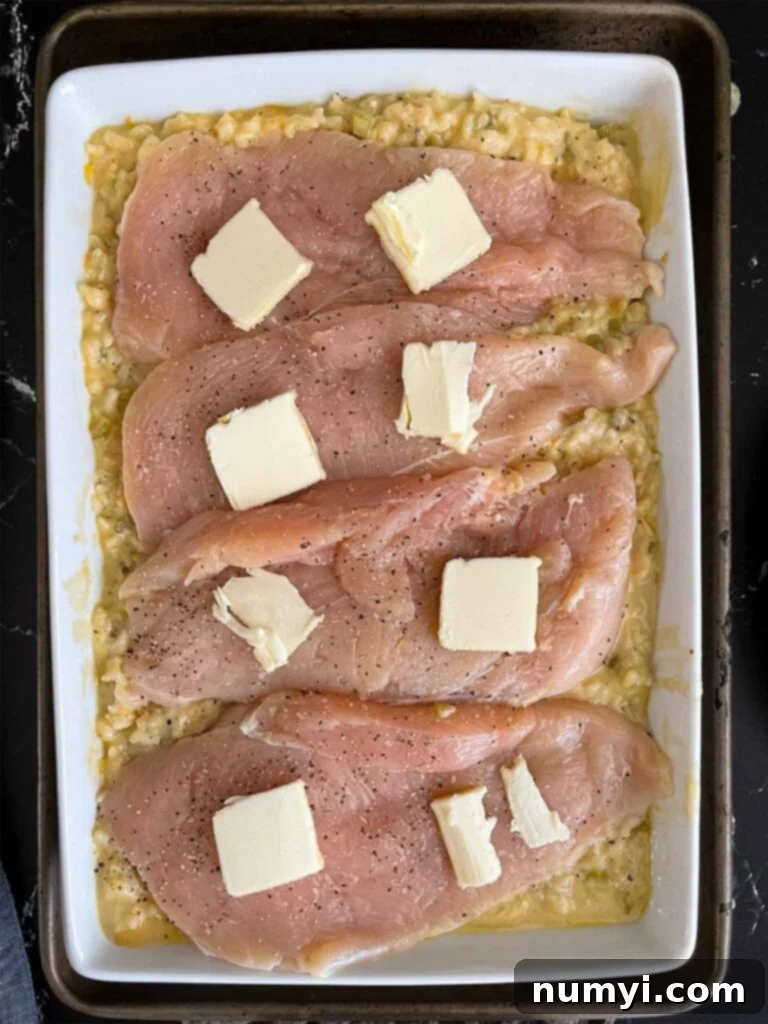 Chicken breast halves topped with pat of butter on top of the rice mixture.