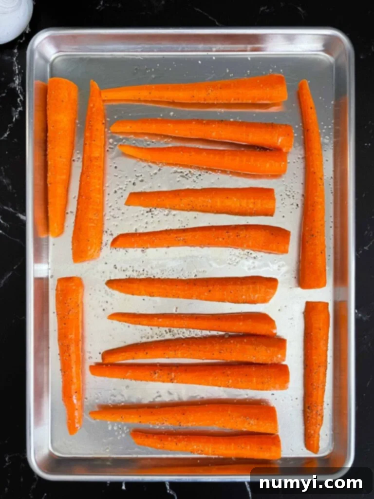 Sweet & Savory Roasted Whole Carrots 4 Raw whole carrots tossed in oil and seasonings on a metal rimmed baking sheet.